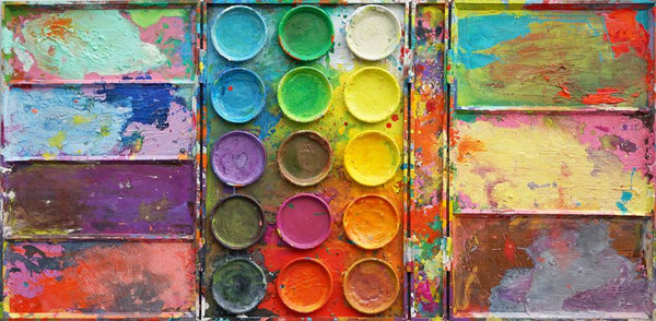 "Die Reise" zeigt bunte Malerei auf einem überdimensionierten Farbkasten (100 x 200 x 4 cm). In den Mischfächer (außen) sind blaue, violette, grüne, gelbe und graue Farben zu sehen. In der Mitte befinden sich 15 Farbteller mit den üblichen Farben einer Palette. In den Zwischenräumen sind Farbkleckse und -flecken sichtbar. Großformatige Kunst. ARTLET | Atelier Hellbusch