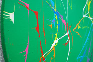 Gemälde Splash 47: Runde Leinwand mit grünem Hintergrund und dynamischen, bunten Farbspritzern in Weiß, Rot, Gelb, Blau und Orange. Zeitgenössische, abstrakte Kunst und experimentelle Technik von 2024 (Seitenaufnahme). ARTLET - Atelier Hellbusch