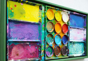 "Jungle" zeigt abstrakte Malerei auf dem Farbkasten (Seitenperspektive) und ergibt ein Wandobjekt. In den Mischfächern (rechts) sind blaue und weiße Farbtöne zu erkennen. Ganz links Gelb, Violett und Bordeaux. In der Mitte befinden sich 12 Farbteller mit den typischen Farben der Palette. In den Zwischenräumen sind Farbkleckse und -flecken sichtbar. Es wurde experimentell gemalt. Moderne Kunst. ARTLET | Atelier Hellbusch.