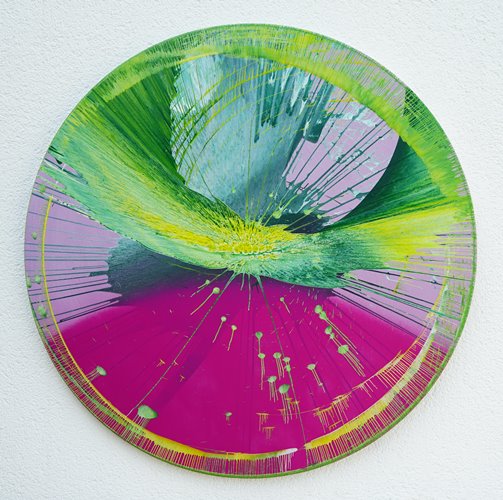 Splash 32 | Experimentelle Kunst mit bunten Farben. Malerei auf runde Leinwand mit einem Durchmesser von 100 cm. Das Gemälde ist bunt mit Grün und Violett als dominante Farbe. Außerdem sind Magenta, Gelb und Weiß in einer schwungvollen, abstrakten Komposition zu sehen. Die Malerei ist durch Farbwürfe entstanden. Präsentiert und fotographiert an der Außenmauer des Ateliers Hellbusch. Experimentelle Kunst. ARTLET | Atelier Hellbusch