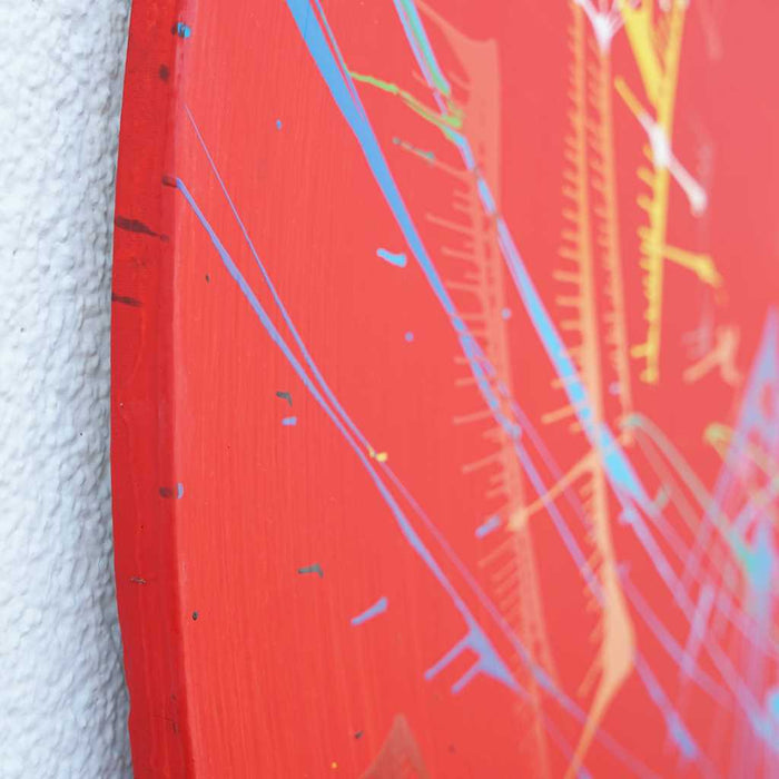 Modernes, rundes Bild Splash 55 (Seitenansicht): Rote Leinwand mit dynamischen Farbspritzern in Blau, Grün, Gelb, Orange und Weiß. Zeitgenössische, abstrakte Kunst von Mark Hellbusch, 2024.