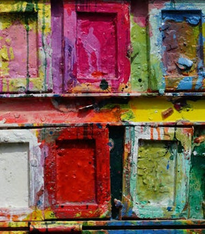 "Der Abschied" zeigt abstrakte Malerei auf einem großen Farbkasten (92 x 112 x 4 cm) - hier in der Nahaufaufnahme. In den Mischfächer (oben) sind Gelb, Blau, Grün, Rot, Schwarz und Ocker zu sehen. Unten befinden sich 16 quadratische Teller mit den üblichen Farben eines Farbkastens. In den Zwischenräumen sind Kleckse und Flecken sichtbar. Moderne Kunst vom Künstler Mark Hellbusch. ARTLET | Atelier Hellbusch