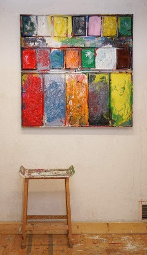 "Gesprächsrunde" zeigt Malerei auf einem überdimensionierten Farbkasten (101 x 101 x 4 cm). In den Mischfächer (unten) sind blaue, orangene, gelbe, rote und violette Farben zu sehen. Oben befinden sich 12 Farbteller mit den üblichen Farben eines Farbkastens. In den Zwischenräumen sind Farbkleckse und -flecken sichtbar. Großformatige Kunst. ARTLET | Atelier Hellbusch